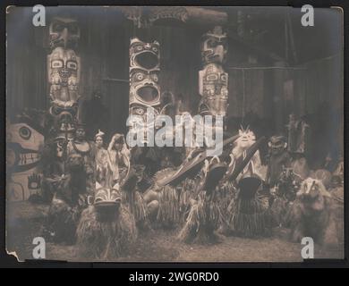 Danseurs masqués-Qagyuhl, c1914. Pendant la cérémonie d'hiver, les danseurs Kwakiutl portant des masques et des costumes, s'accroupissent au premier plan avec d'autres derrière eux. Le chef à l'extrême gauche tient le bâton d'un orateur. Trois totems en arrière-plan. Banque D'Images