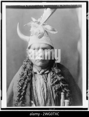 Oyegi-a YE ("Frost Moving"), gouverneur de Santa Clara, c1905. Oyegi-a YE, portrait tête et épaules, face à l'avant, coiffé d'une casquette avec plumes et une seule corne. Banque D'Images