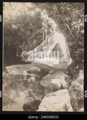 Rêves de jour, 1905. La photographie montre le chef Plenty coups accroupi sur la roche près de l'étang, les doigts entrelacés, méditant. Banque D'Images