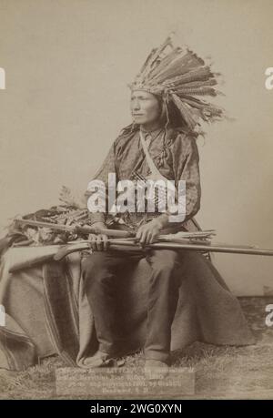 Little, l'instigateur de la révolte indienne à Pine Ridge, 1890 [] /, 1890, c1891. Little, chef de groupe Oglala, portrait studio en pied, assis, orienté à gauche, porter une coiffe en plume de dinde, tenir un fusil et un arc et des flèches sur les genoux. Banque D'Images