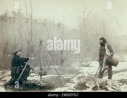 Chasse au cerf. Une chasse au cerf près de Deadwood en hiver 87 et 88. Deux mineurs McMillan et Hubbard ont obtenu leur jeu []. Deux chasseurs autour du feu de camp ; un cuisinant, l'autre tenant un cerf mort sur son épaule. Banque D'Images