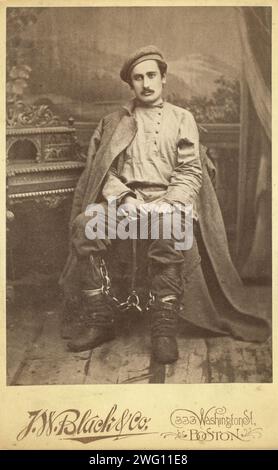 Portrait en pied d'un homme en vêtements de prisonnier et fers à jambes, assis, face à l'avant, entre 1880 et 1886. Inscription au verso : Sukhomlin en tenue de prisonnier (photo de police). Banque D'Images