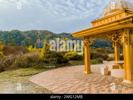 Gazebo de couleur dorée avec un feuillage luxuriant avec un mât de drapeau derrière un parapluie bleu sous un ciel nuageux à Daejeon, Corée du Sud Banque D'Images