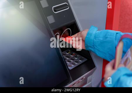 Femme en veste bleue insérant sa carte de crédit dans un guichet automatique pour retirer de l'argent Banque D'Images