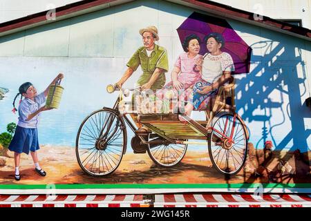 Une murale dans la ville de Phuket, Phuket, Thaïlande, représentant un conducteur de trishaw vieux avec deux passagers féminins et une jeune fille avec une boîte à tiffin (boîte à lunch) Banque D'Images