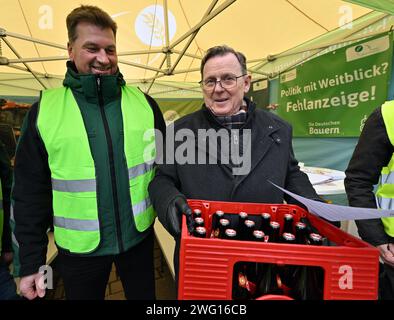 02 février 2024, Thuringe, Erfurt : Bodo Ramelow (r, Die Linke), ministre-président de Thuringe, visite le camp des agriculteurs de l'Association des Thuringe devant le Parlement de l'État de Thuringe et emporte une caisse de bière. Lars Fliege (l), vice-président de l'Association des agriculteurs de Thuringe, avait fait un pari avec le ministre de l'Agriculture de Thuringe pour une caisse de bière, perdu et remis le pari à Ramelow. En marge de la session de trois jours du Parlement de l'État de Thuringe, les agriculteurs demandent l'annulation de la réduction du diesel agricole, une exonération fiscale pour les biocarburants et un redu Banque D'Images