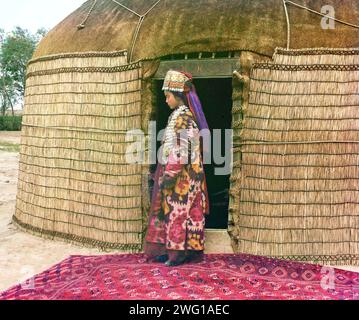 Portrait de profil en pied d'une femme, peut-être turkmène ou kirgiz, debout sur un tapis à l'entrée d'une yourte, vêtue de vêtements et de bijoux traditionnels, entre 1905 et 1915. Diversité ethnique : profil d'un nomade. Dans ce portrait, Prokudin-Gorksii capture la robe traditionnelle, les bijoux et la coiffure d'une femme ouzbèke. Une yourte est une tente portative utilisée comme logement par les peuples nomades d'Asie centrale. Après avoir conquis le Turkestan au milieu des années 1800, le gouvernement russe a exercé une forte pression sur les peuples nomades pour adopter un mode de vie sédentaire et s'installer définitivement dans les villages Banque D'Images