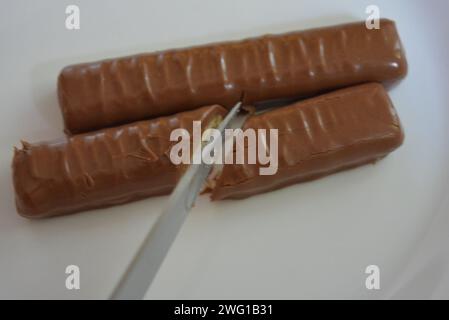 Bonbons, bâtonnets coupés au couteau recouverts de chocolat au lait, de foie sablé et de caramel placés sur une assiette en verre blanc. Banque D'Images