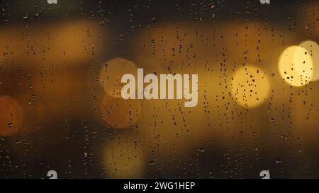 Une photo floue de gouttes de pluie sur une surface de verre avec une lumière chatoyante. Banque D'Images