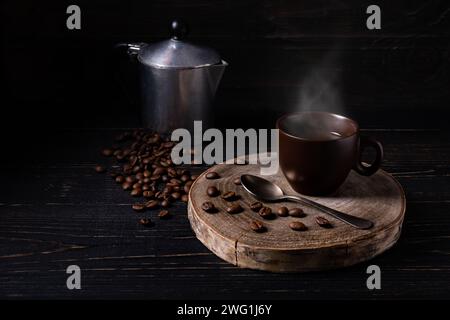 Sur fond de bois sombre, grains de café torréfiés, une cafetière italienne et une tasse de café noir chaud Banque D'Images