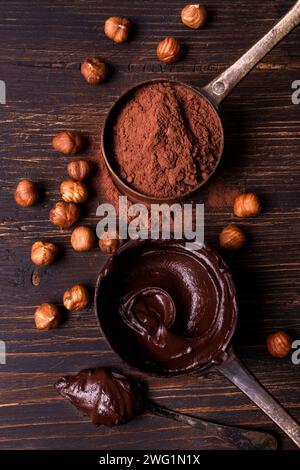 Au premier plan, vue de dessus, sur un fond de bois brut, cuillères à mesurer en métal vintage avec chocolat noir fondu et poudre de cacao avec HAZ décortiqué Banque D'Images