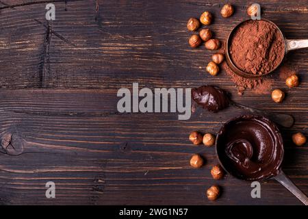 Au premier plan, vue de dessus, sur un fond de bois brut, cuillères à mesurer en métal vintage avec chocolat noir fondu et poudre de cacao avec HAZ décortiqué Banque D'Images