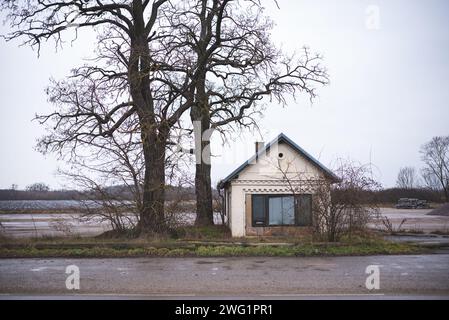 Vieille maison abandonnée sur le bord d'un emplacement de stockage en hiver. Deux grands arbres sans feuilles à côté du bâtiment Banque D'Images