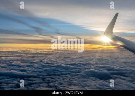 Vue depuis une fenêtre d'avion sur une mer de nuages au coucher du soleil avec l'aile de l'avion Banque D'Images