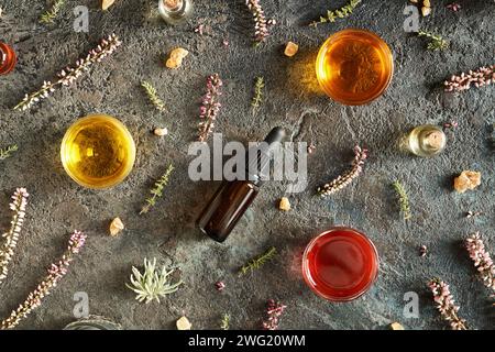 Fond sombre avec des bouteilles et des bols d'huile essentielle d'aromathérapie avec encens, thym et fleurs de bruyère Banque D'Images