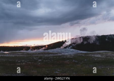 La vapeur s'élève du geyser Old Faithful sous un ciel couvert au coucher du soleil dans le parc national de Yellowstone Banque D'Images