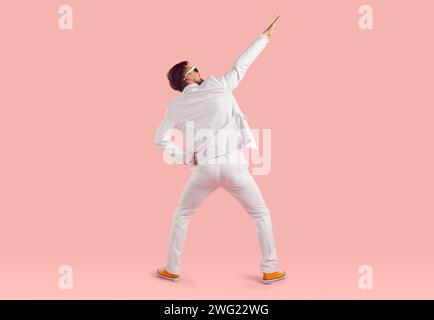 Vue arrière d'un jeune homme heureux et drôle dans un costume blanc dansant dans le studio de mode Banque D'Images