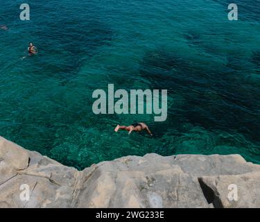 Un homme saute dans la mer des rochers sur une plage privée à Valetta, Malte en été. Banque D'Images