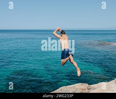 Un homme saute dans la mer des rochers sur une plage privée à Valetta, Malte en été. Banque D'Images