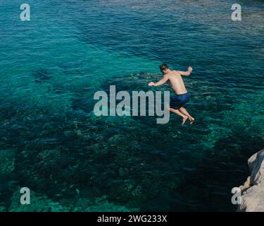 Un homme saute dans la mer des rochers sur une plage privée à Valetta, Malte en été. Banque D'Images