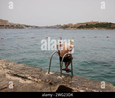 Un nageur se prépare à entrer dans la mer à la plage de Tigne point, Malte. La Valette peut être vue en arrière-plan. Banque D'Images