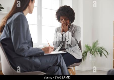 Femme assise avec un psychologue, pleurant et couvrant le visage avec les mains pendant une séance de thérapie. Banque D'Images