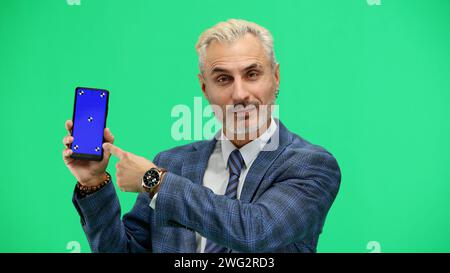 Un homme, en gros plan, sur fond vert, montre un téléphone Banque D'Images