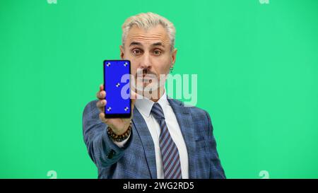 Un homme, en gros plan, sur fond vert, montre un téléphone. Banque D'Images