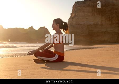 Femme sportive assise sur la plage méditant. Refroidissement du surfeur ou du nageur. Banque D'Images