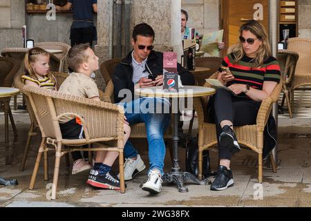Gérone, Espagne — 31 mai 2023. Une famille s’arrête dans un café extérieur à Gérone ; les parents vérifient leurs téléphones portables pendant que les enfants attendent. Banque D'Images