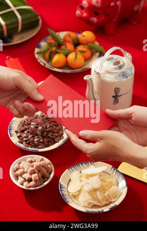 Une table décorée en rouge pour la célébration du nouvel an lunaire avec de la nourriture et des boissons. Les gens se donnent de l'argent chanceux Banque D'Images