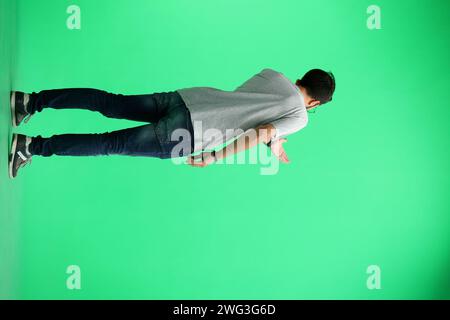 Un homme, sur fond vert, en pleine hauteur, regarde sa montre Banque D'Images