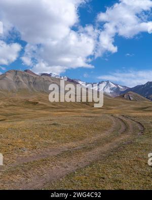 Piste de terre dans les pâturages d'été dans la vallée de Sary Tash, Kirghizistan avec fond de chaîne de montagnes TRANS-Alay enneigée le long de l'autoroute de haute altitude du Pamir Banque D'Images