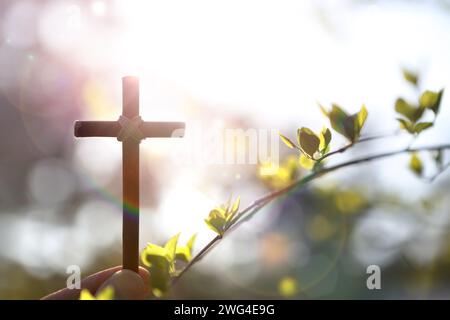Fond avec des fleurs et des bourgeons de forsythia jaunes et la sainte croix de Jésus-Christ en main un jour chaud de printemps avec une forte lumière du soleil Banque D'Images