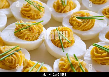 Gros plan d'œufs farcis avec deux brins de ciboulette sur une assiette blanche sur une table en bois. Banque D'Images