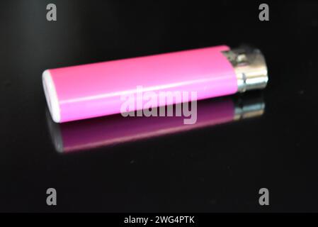 Un briquet en plastique rose repose sur une surface noire brillante. Banque D'Images