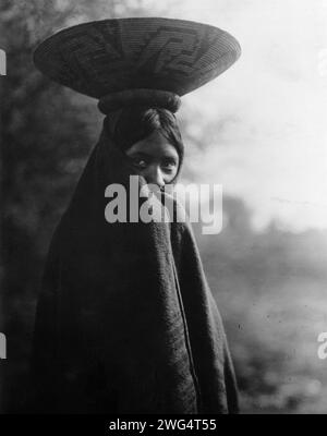 Maricopa fille, portrait demi-longueur, debout, face légèrement à droite, enveloppé dans une couverture, avec plateau panier sur la tête, c1907. Banque D'Images