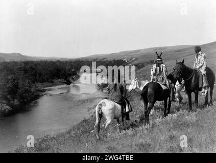 Trois Indiens Piegan et quatre chevaux sur une colline au-dessus de la rivière, c1910. Banque D'Images