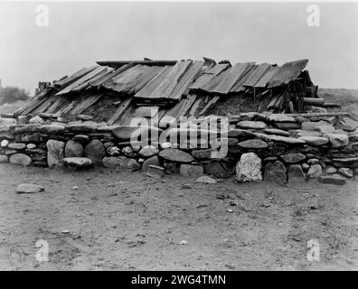 Hupa maison de sueur, 1923. Bâtiment souterrain recouvert d'un toit en planches de bois, entouré d'un mur de gros rochers. Banque D'Images