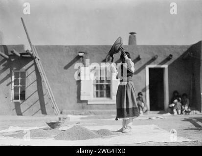 Vendange du blé, c1905. Femme Tewa remuant du blé devant le bâtiment pueblo. Banque D'Images