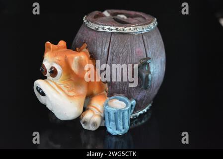 Statuette en céramique, une tirelire pour l'argent sous la forme d'un chien regardant hors d'une cabine en forme de tonneau avec de la bière sous la surface noire brillante. Banque D'Images