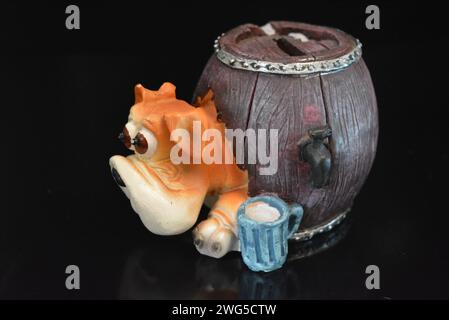 Statuette en céramique, une tirelire pour l'argent sous la forme d'un chien regardant hors d'une cabine en forme de tonneau avec de la bière sous la surface noire brillante. Banque D'Images