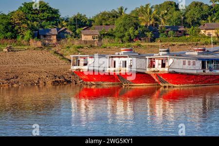 trois bateaux en bois blanc et rouge sur la rive d'une rivière avec un petit village Banque D'Images