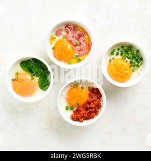 Oeufs en cocotte (oeufs cuits au four) dans des ramequins sur fond clair. Concept d'alimentation saine. Vue de dessus, pose à plat Banque D'Images