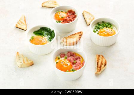 Oeufs en cocotte (oeufs cuits au four) dans des ramequins et des toasts sur fond clair. Plat pour petit déjeuner ou déjeuner sain. Vue rapprochée Banque D'Images