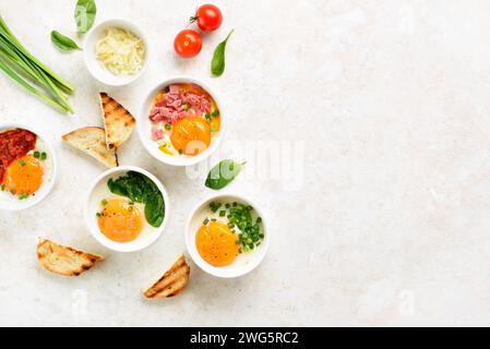 Oeufs en cocotte (oeufs cuits au four) en portion bol en céramique sur fond clair avec espace libre. Concept de nourriture saine du matin. Vue de dessus, pose à plat Banque D'Images