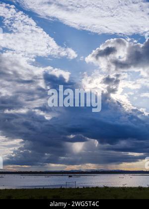 Des nuages de tempête dramatiques sur le lac avec des averses de pluie et des rayons de lumière éthérés transperçant la tempête, le ciel avant la pluie. Nuages d'orage au-dessus de l'ouate Banque D'Images