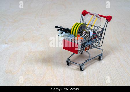 Un panier avec pièces et composants électriques. Bornes, ampoule, ruban isolant, serre-câbles. Concept : magasin de produits électriques. Dos en bois Banque D'Images