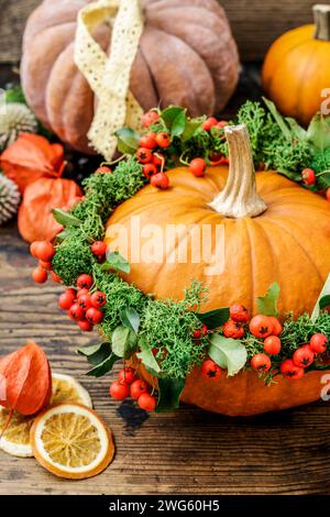 Décoration de citrouille avec couronne aux fruits rouges (cotoneaster horizontalis) et de mousse verte. Bougies et les fruits secs sur la table. Banque D'Images