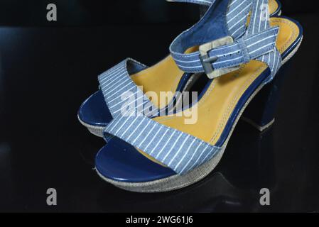 Chaussures femme élégantes et inhabituelles en cuir verni bleu véritable et tissu bleu. Sandales, sandales, chaussures de vol sont situés sur un noir brillant. Banque D'Images